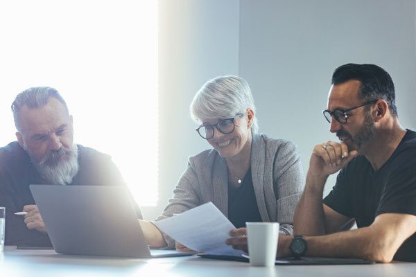 A photo of people sitting in an office looking at a laptop together, used for the "Why Self-Funded Medical Group Captives Are a Safe Bet" post