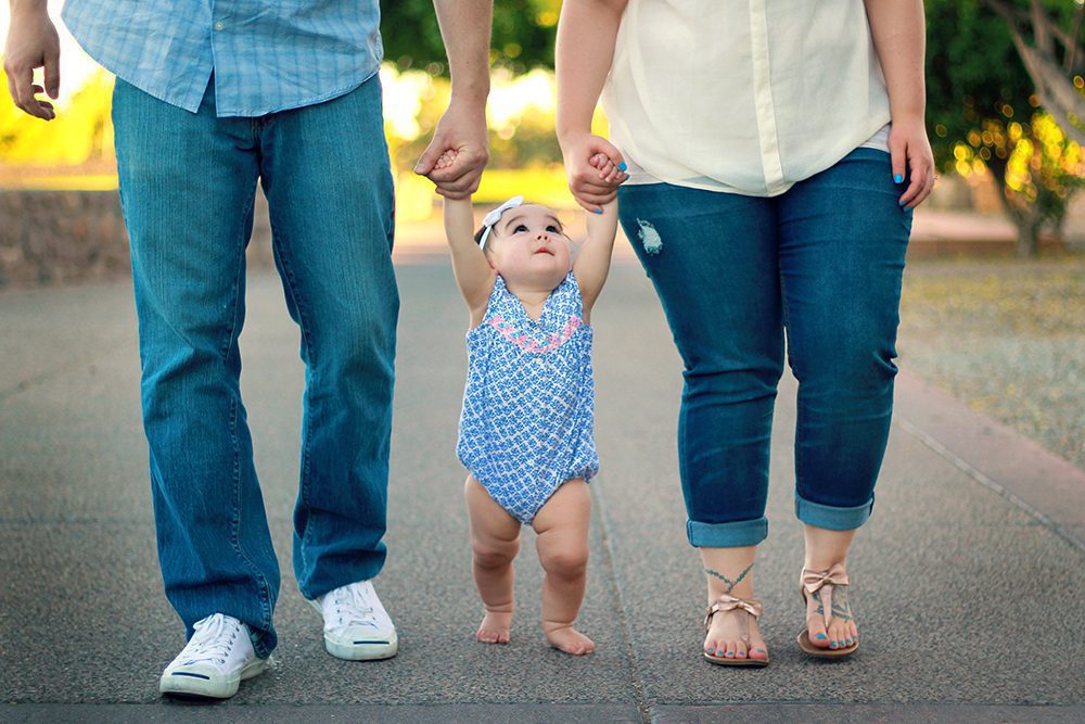 Family-FredCChurch Baby learning how to walk, holding hands of parents and looking up at them
