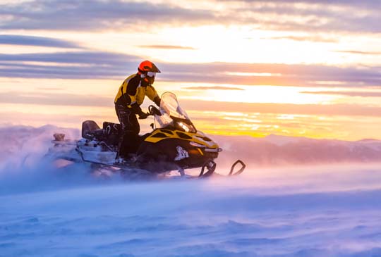 A person snowmobiling with a beautiful bright sky in the back