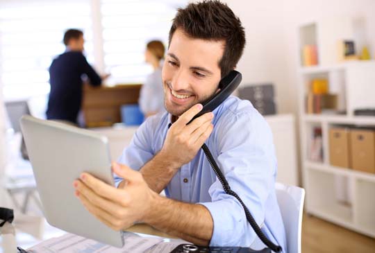 A man smiling and on the phone while holding and looking at his iPad