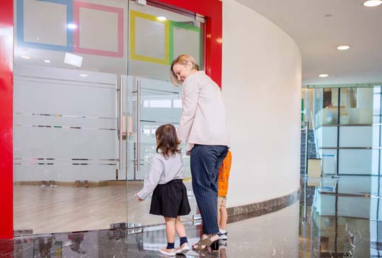 An adult holding hands with little children as they enter a building