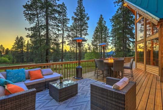 A deck with a couch, a table, a taller table with seats surrounded by a fire, and outdoor heating lamps