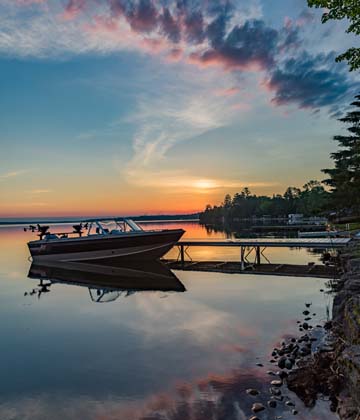 A small boat docked in the water with a beautiful sunset in the background