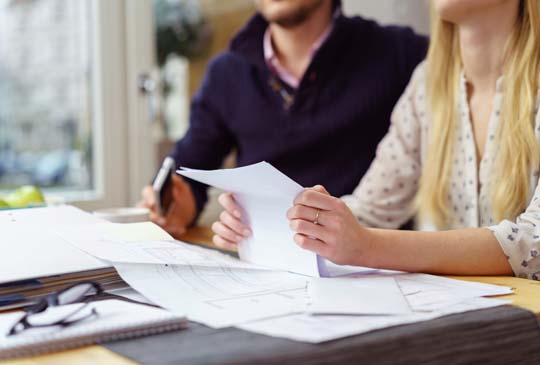 A couple sitting at a messy table filled with papers with the woman holding one piece of paper