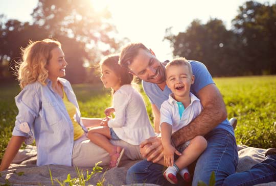 A family sitting outside on the grass smiling and laughing at each other