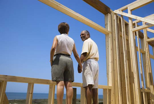 An older couple holding hands and smiling while standing in an unfinished house