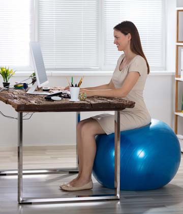 A woman sitting on a yoga ball while completing work at her desk