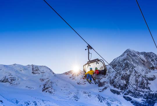 Snow-covered mountains with two people on a ski lift