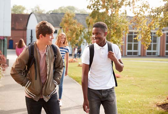 Two boys walking down the sidewalk with their backpacks on smiling at each other