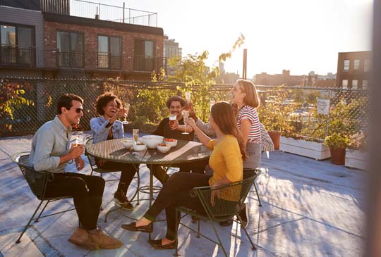 Group of people laughing and sitting at a table outside while giving cheers with their drinks in hand